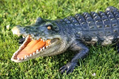 Açık ağızlı, gerçekçi detaylara sahip timsah heykeli çim üzerinde duruyor.