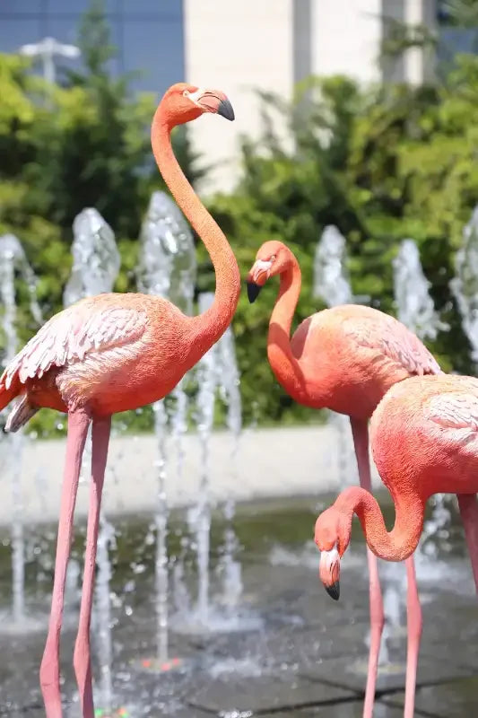 Fıskiyeli bahçede duran üç pembe flamingo heykeli, dekoratif dış mekan sanat eseri