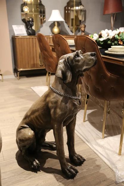 İç mekanda oturan weimaraner cinsi köpek heykeli, dekoratif masa ve sandalyeler önünde